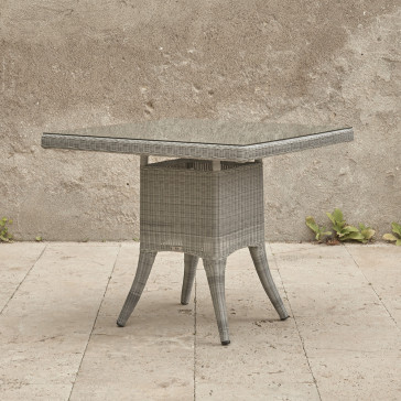 Four seater grey rattan garden table at an angle in front of stone wall