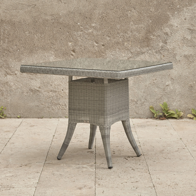 Four seater grey rattan garden table at an angle in front of stone wall