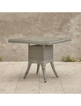 Four seater grey rattan garden table at an angle in front of stone wall