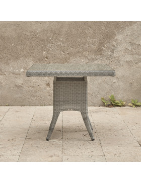 side view of four seater grey rattan garden table in front of stone wall