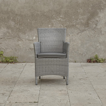 Grey rattan dining chair. On a terrace in front of stone wall font view