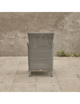 Grey rattan dining chair. On a terrace in front of stone wall back view