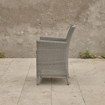 Grey rattan dining chair. On a terrace in front of stone wall side view