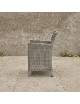 Grey rattan dining chair. On a terrace in front of stone wall side view