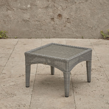 Compact garden rattan side table wirh tempered glass top pictured at an angle on a southern French terrace