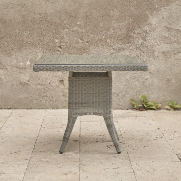 Four seater Grey rattan garden table. On a terrace in front of stone wall