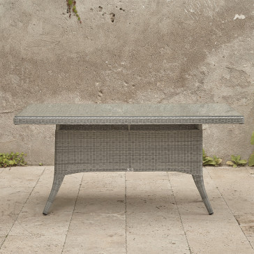 Six seater Grey rattan garden table. On a terrace in front of stone wall