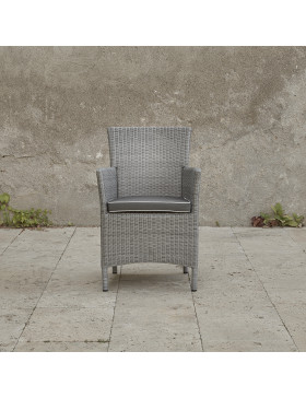 Grey rattan dining chair. On a terrace in front of stone wall