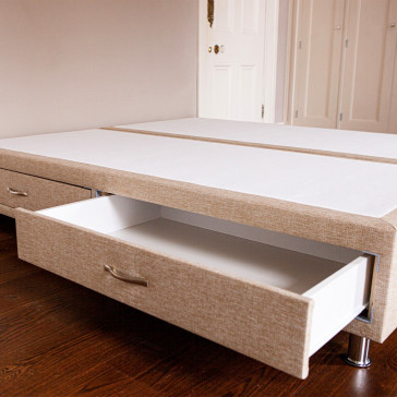 Divan bed base showing both drawers with one drawer open upholstered in an oatmeal furniture fabric pictured on a wooden floor